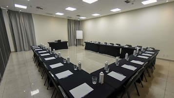 Un salón de conferencias con una mesa larga, sillas, un atril, una pantalla de proyector y botellas de agua.