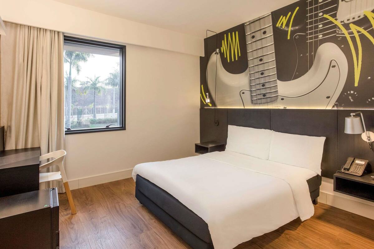 Hotelkamer met een bed, bureau, stoel, raam en een muur met een ontwerp van een muziekinstrument.
