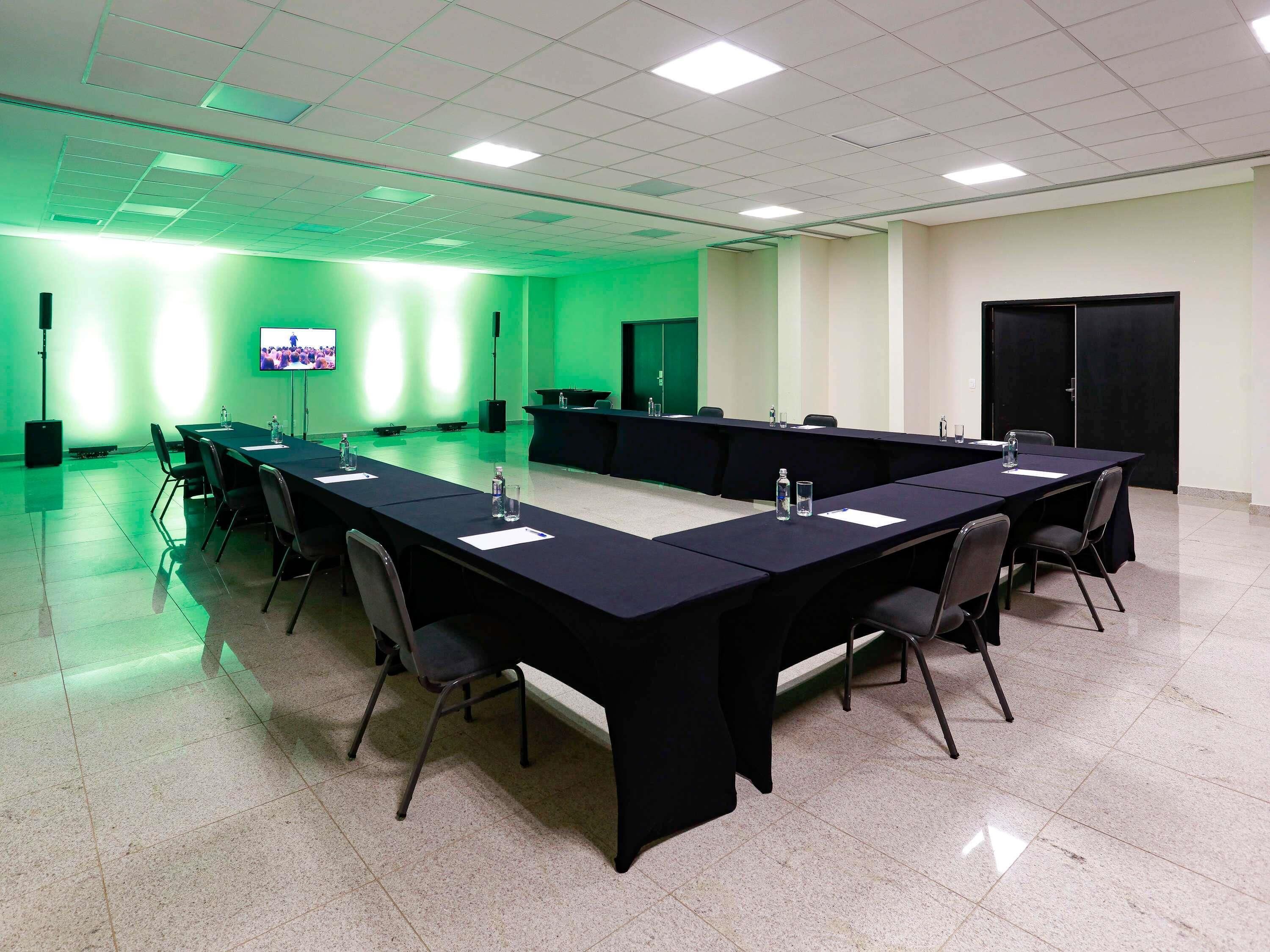 A conference room with a long table, chairs, a TV screen, and a green-lit wall.
