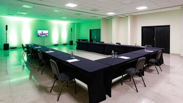 A conference room with a long table, chairs, a TV screen, and a green-lit wall.
