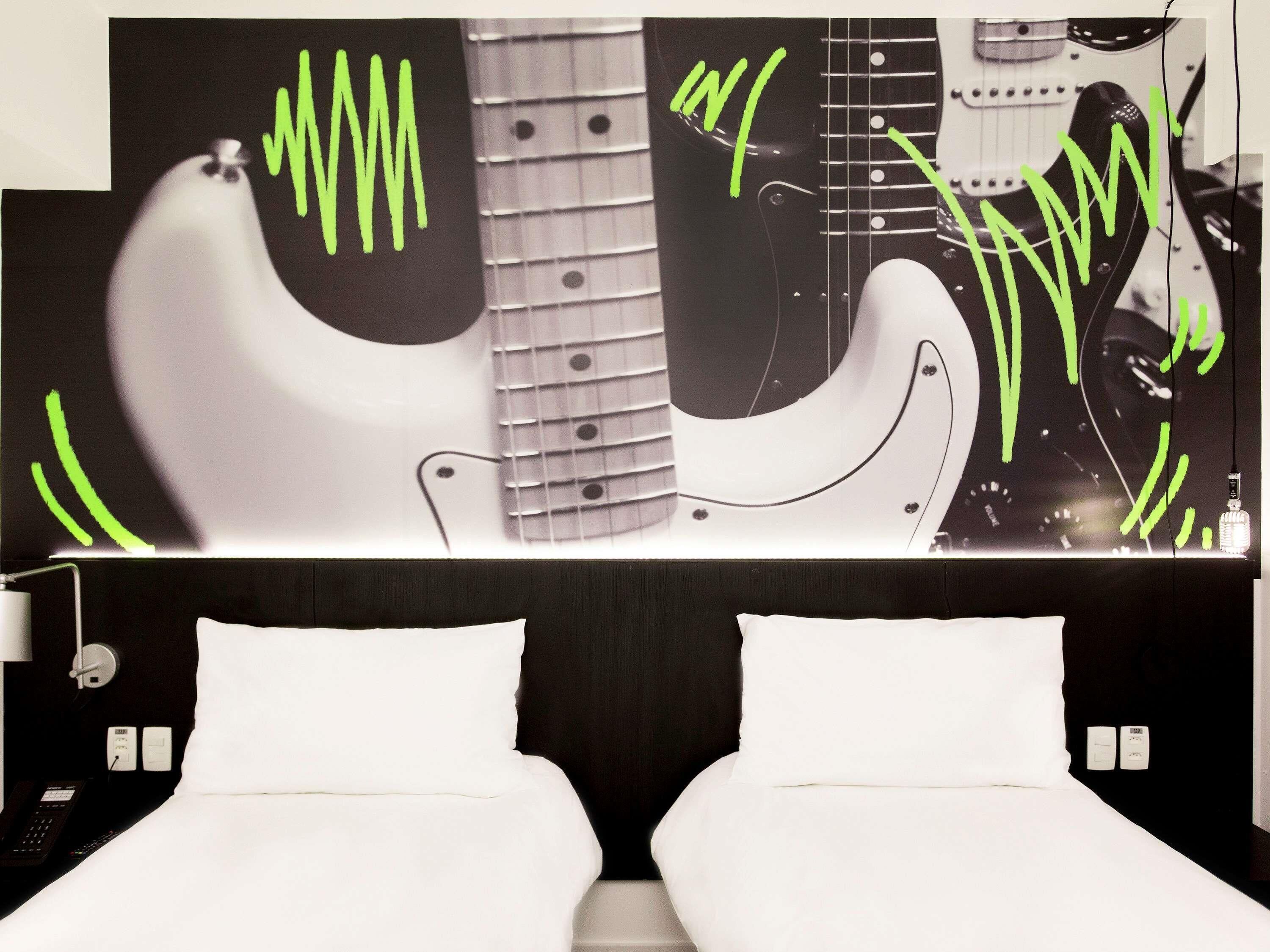 A hotel room with a bed, a bedside table, a lamp, and a large wall decoration.