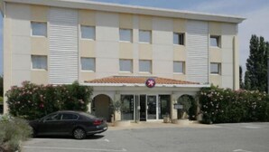 A hotel with a beige facade, a red-tiled roof, and a parking lot with a black car. - The Originals City, Hôtel la Belle Étape, Brignoles (Brignoles)