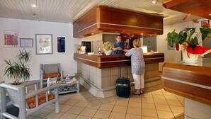 A reception area with a wooden counter, a seating area with a bench, and a potted plant. - The Originals City, Hôtel la Belle Étape, Brignoles (Brignoles)