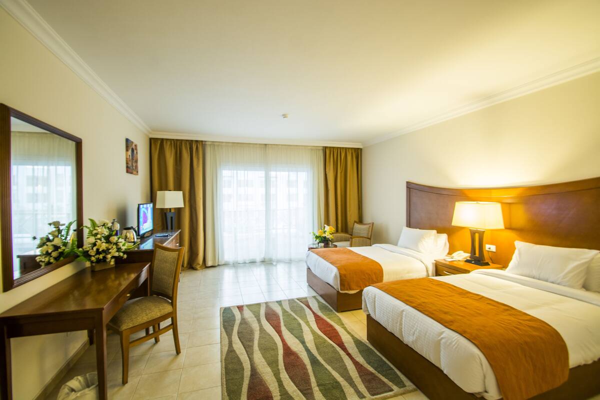A hotel room with two beds, a desk with a computer, a chair, and a large mirror.