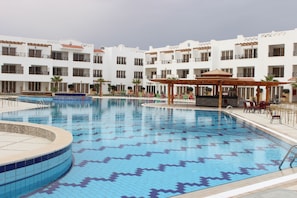Ein Hotel mit Pool, Außenbereich und einer überdachten Liegefläche mit Sonnenschirmen.