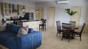 Un salon avec un canapé bleu, une table à manger en bois, des chaises et un coin cuisine équipé de placards et d’appareils électroménagers.