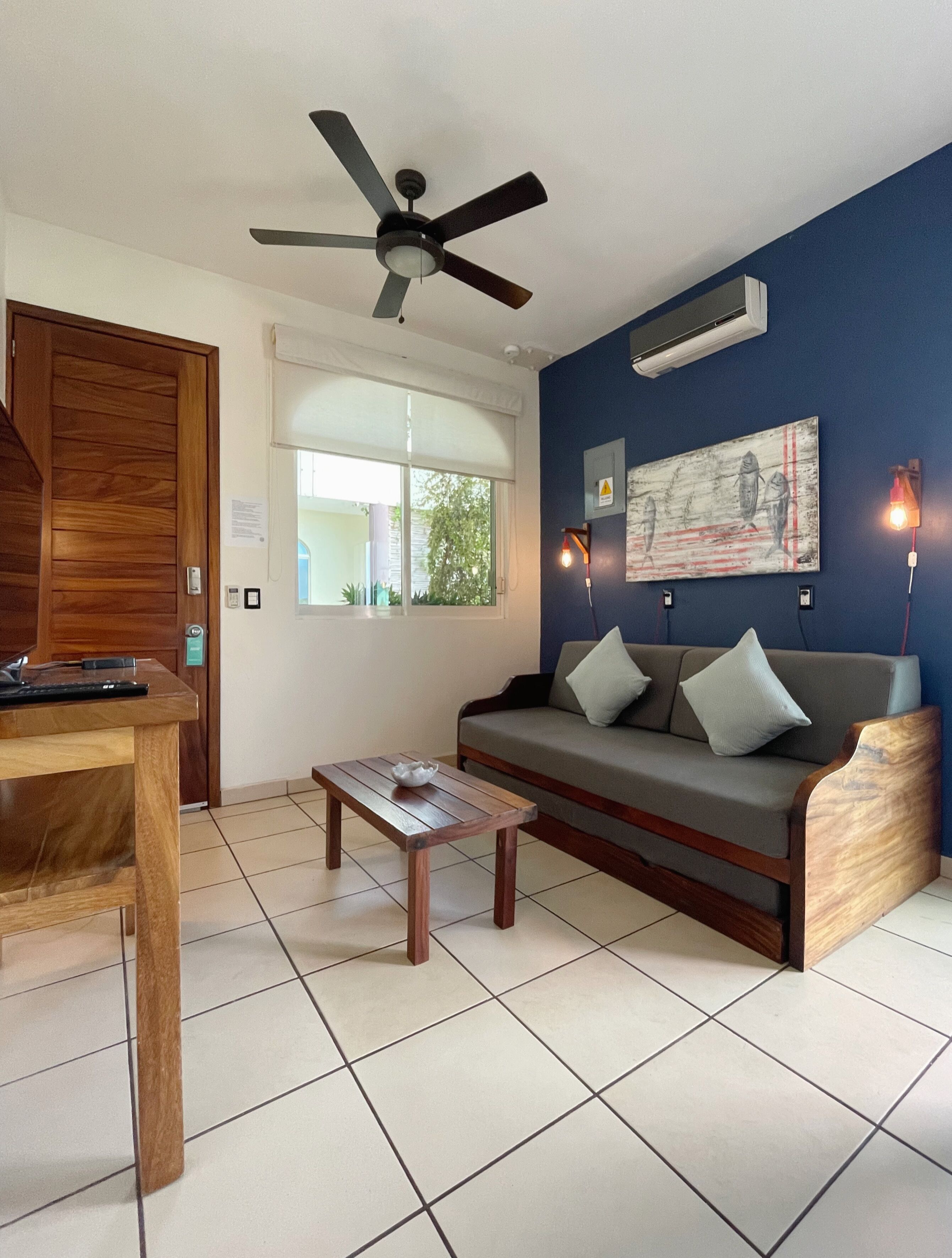 A living room with a wooden table, a sofa, a ceiling fan, and a wall-mounted air conditioner.