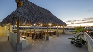 Terraza en la azotea con techo de paja, mobiliario exterior y plantas en macetas.