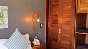 Un dormitorio con cama, mesita de noche, lámpara de pared, armario de madera y un cuadro en la pared.