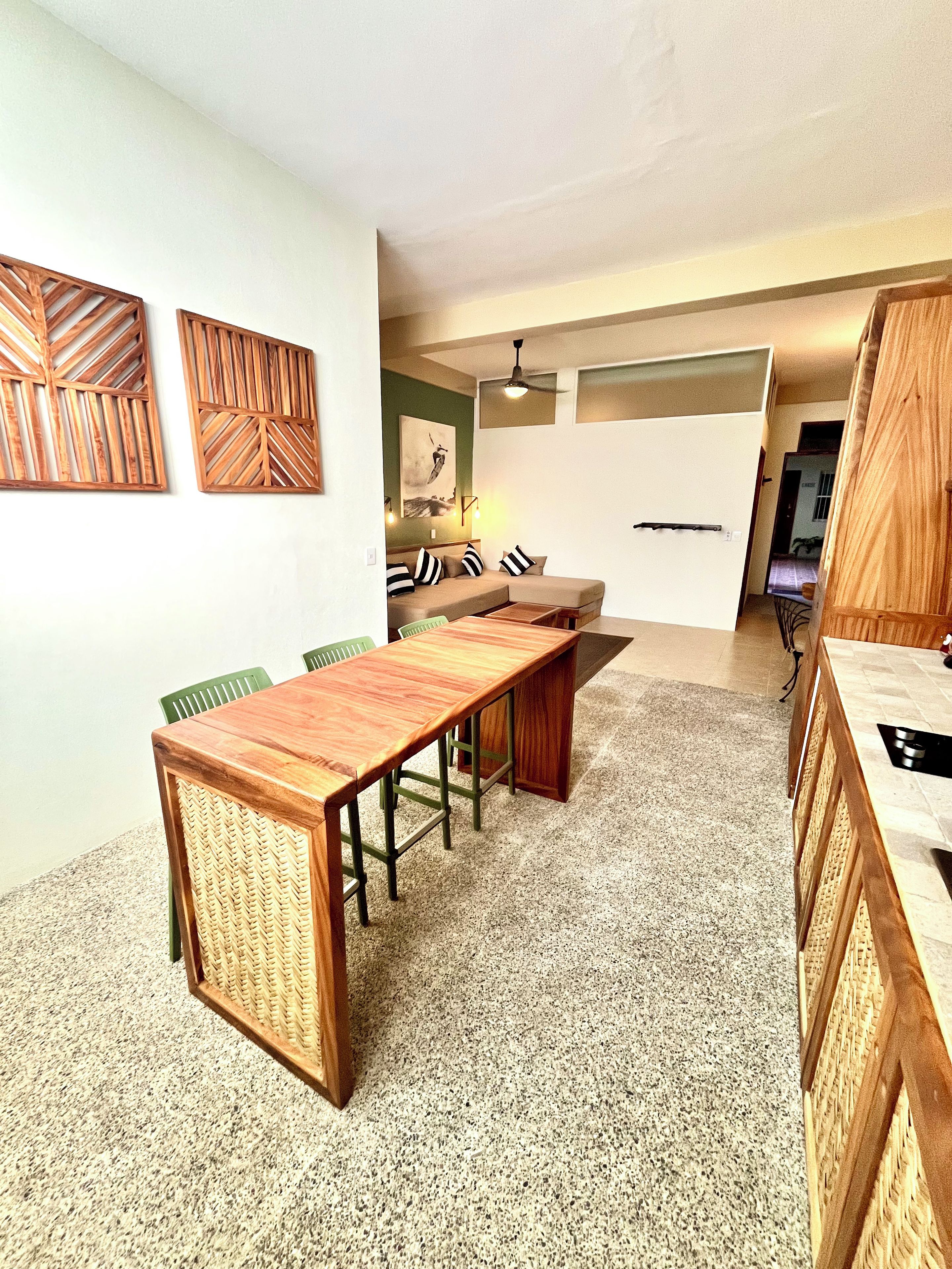 Un comedor con una larga mesa de madera, sillas verdes y un sofá con cojines a rayas.