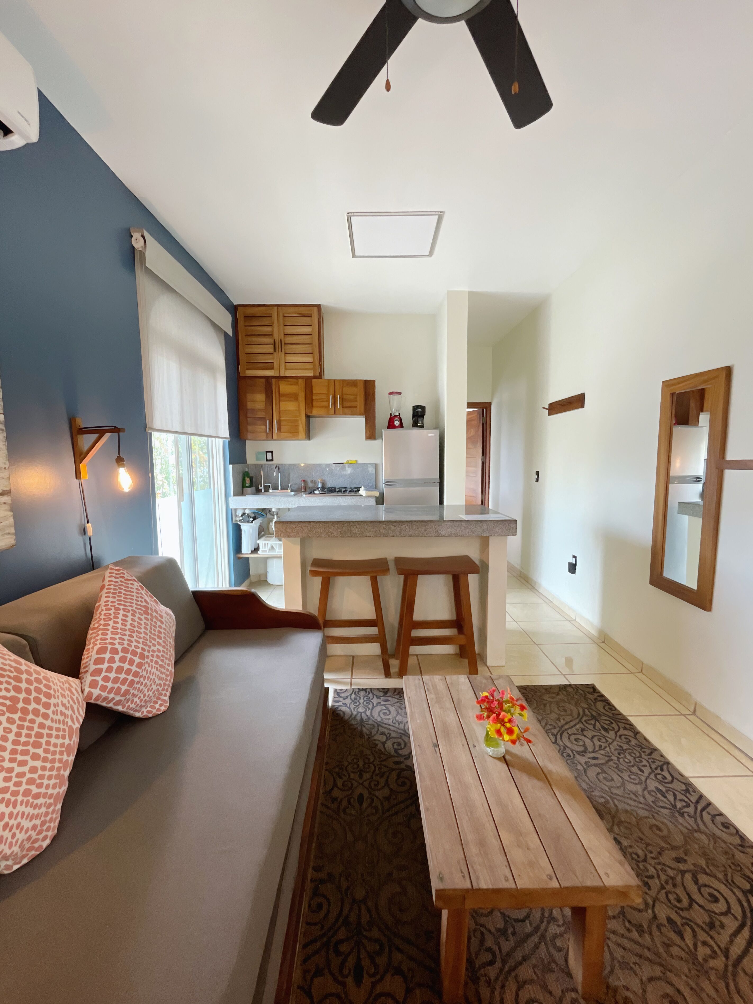 A modern living room with a sofa, a coffee table, and a kitchen area with a refrigerator and a stove.