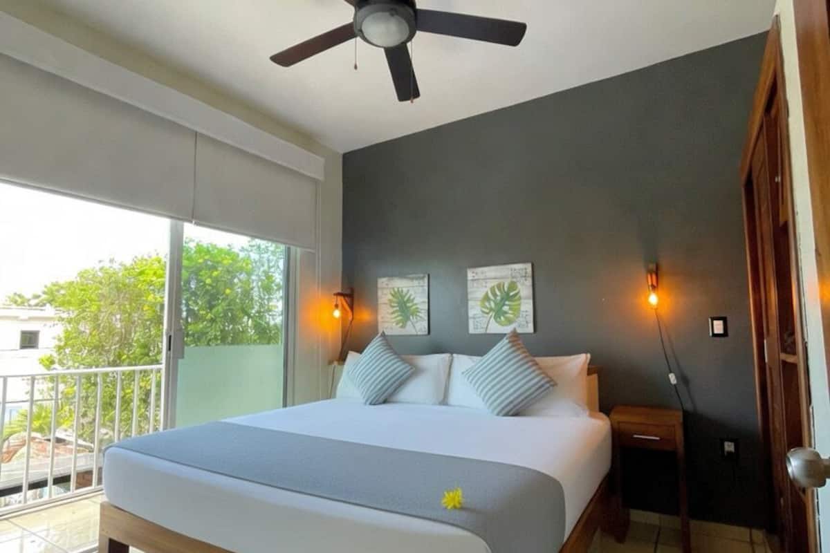 A bedroom with a bed, ceiling fan, wall art, and a balcony.