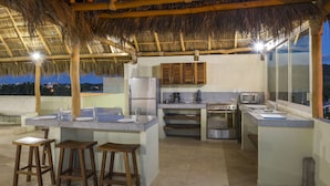 Una cocina con techo de paja, un refrigerador, una estufa y taburetes de bar.