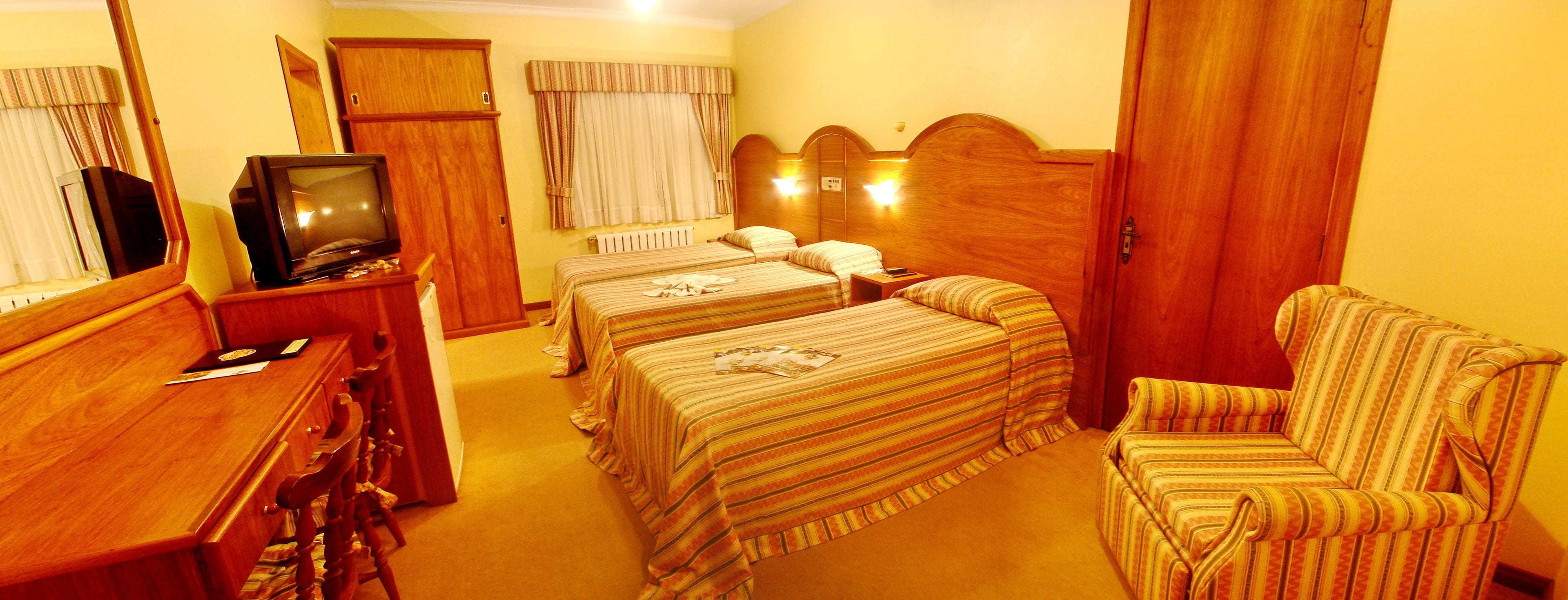 Ein Hotelzimmer mit zwei Einzelbetten, einem Holztisch mit Fernseher, einem Sessel und einem Kleiderschrank.
