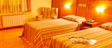 A hotel room with two beds, striped bedding, a wooden headboard, bedside lamps, a nightstand, and a window with curtains.
