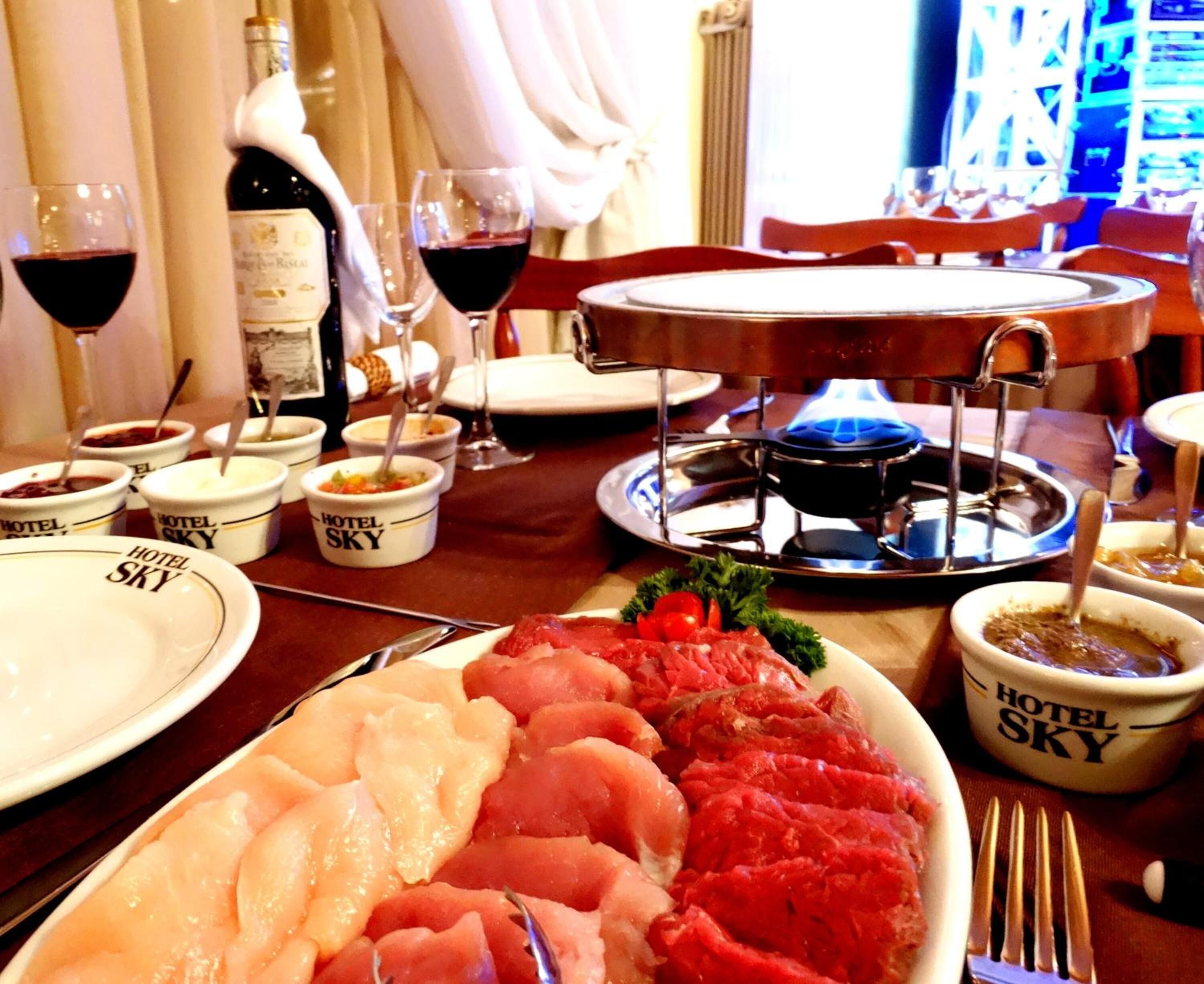Una mesa de comedor con diversos alimentos, como un plato de carne cruda, recipientes con salsas y una botella de vino.