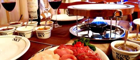 Una mesa de comedor con diversos alimentos, como un plato de carne cruda, recipientes con salsas y una botella de vino.