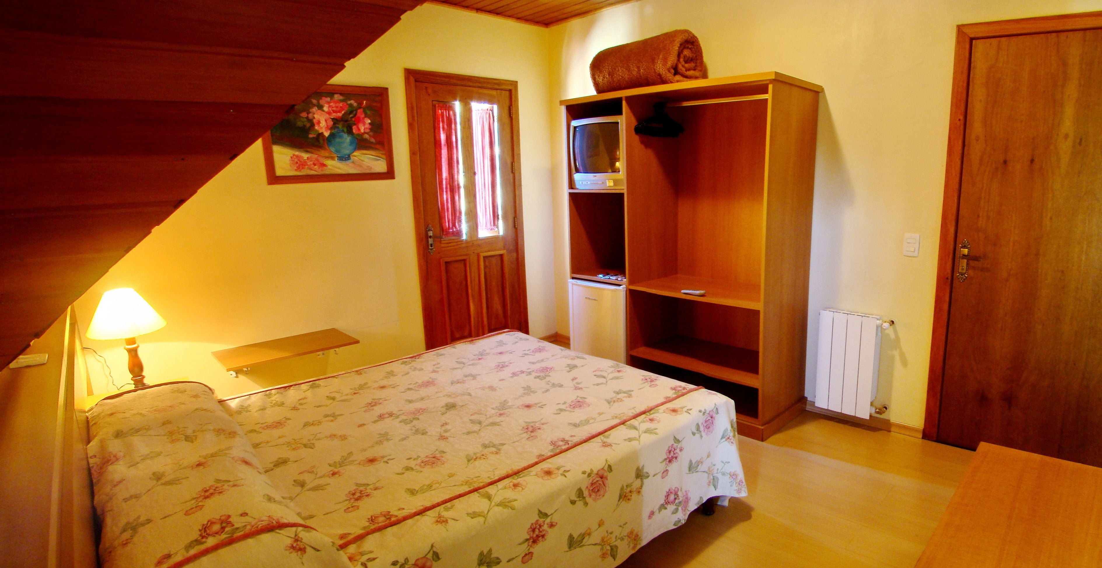 Un dormitorio con cama, armario de madera, televisor y radiador.