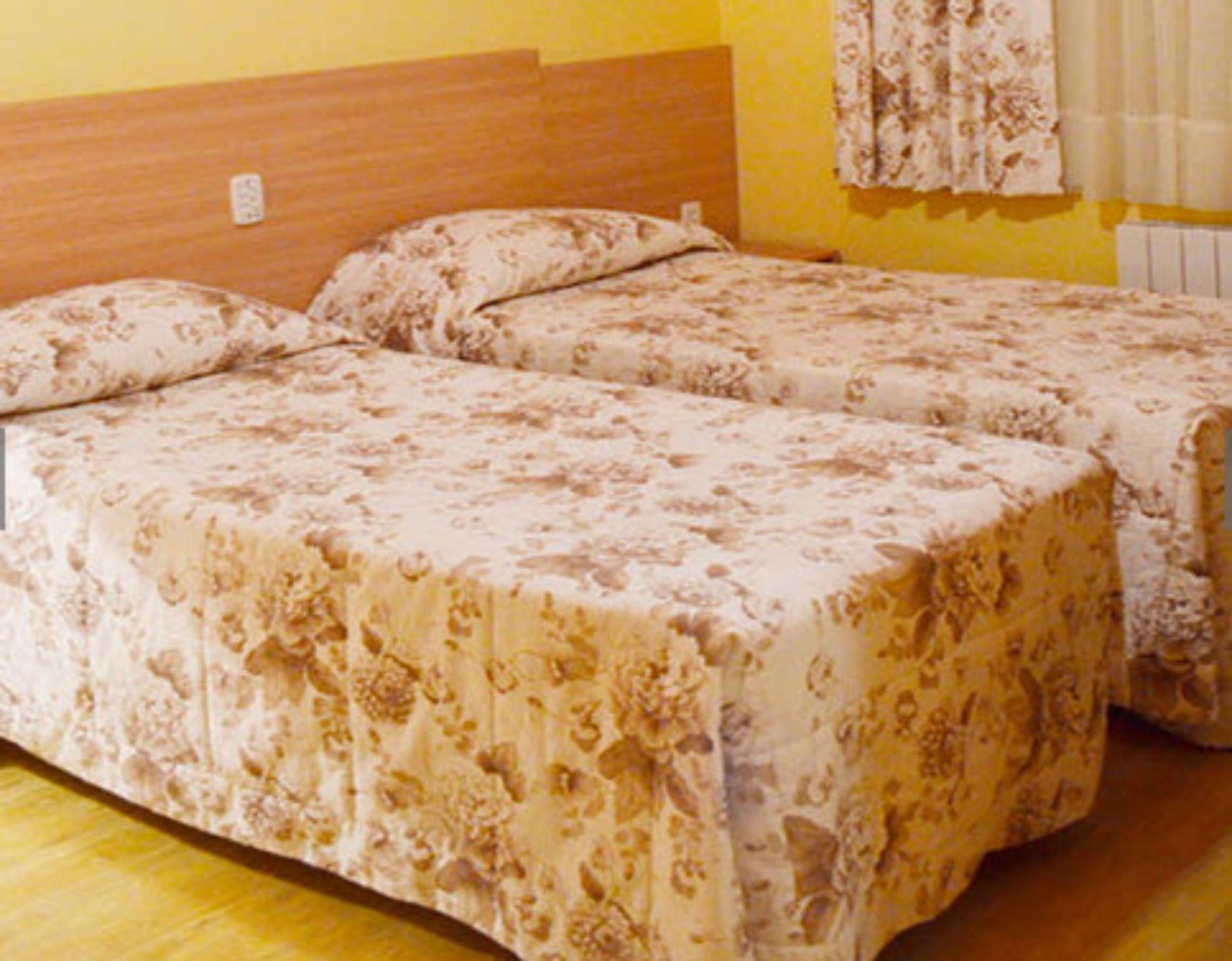A double bed with a floral bedspread in a room with yellow walls and a wooden headboard.