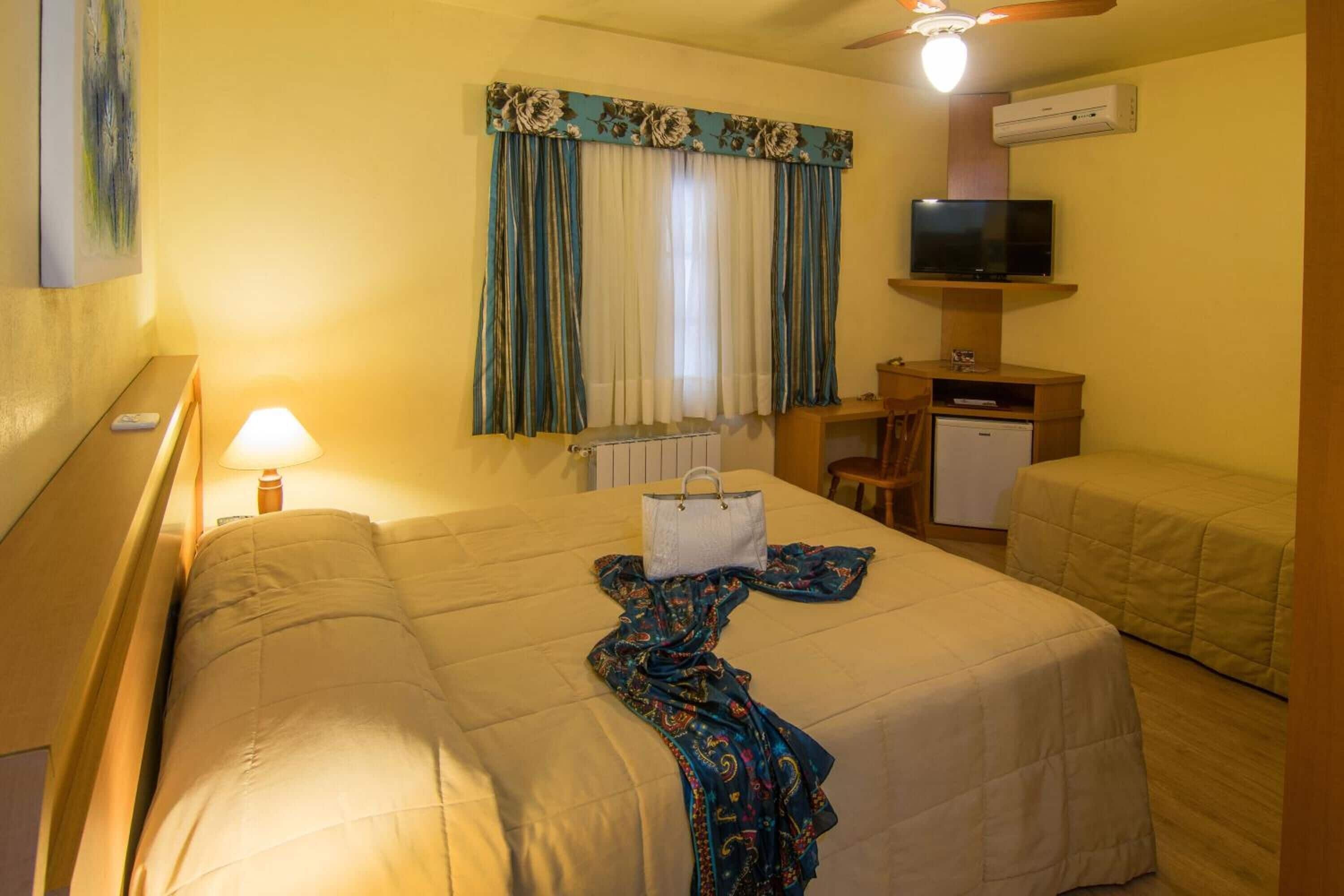 A hotel room with a bed, a desk, a television, and a radiator.