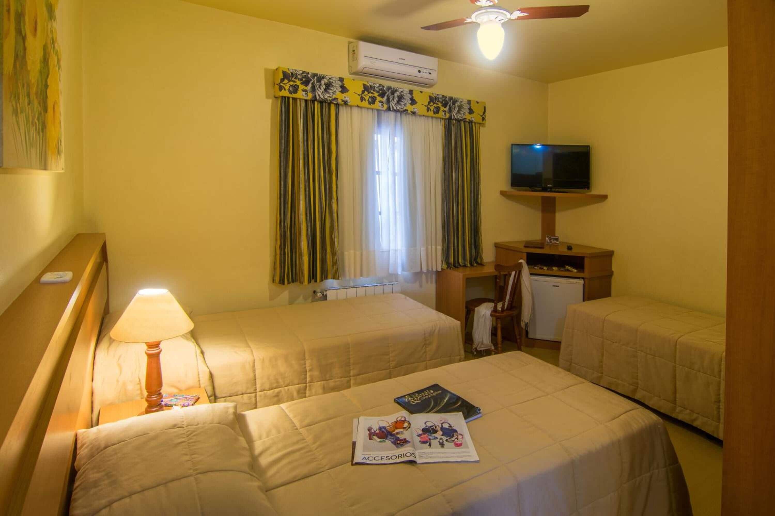 A hotel room with two beds, a television, an air conditioning unit, and a small table with a lamp.