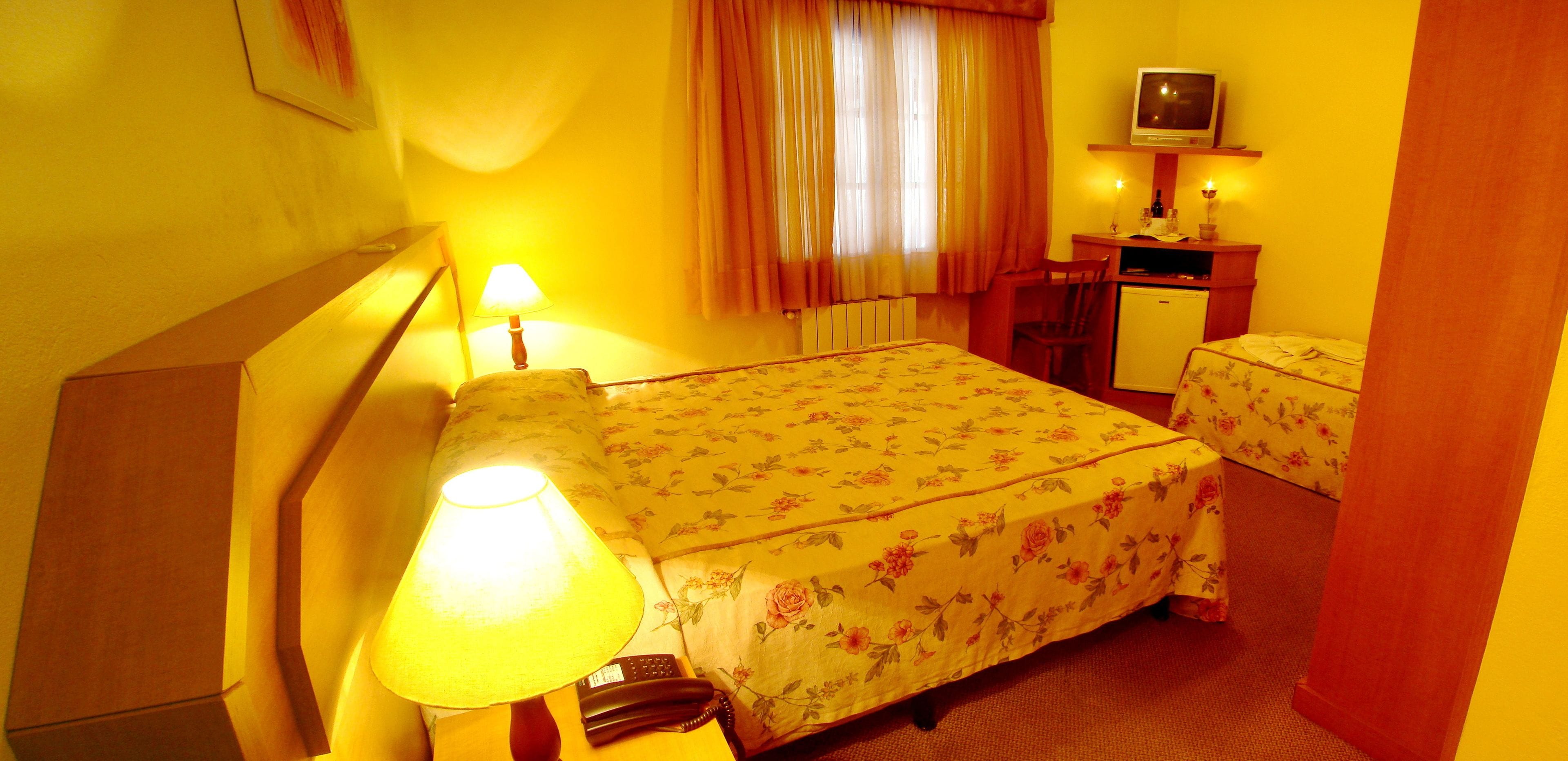 A hotel room with a bed, a desk, a chair, a lamp, a television, and a small table.