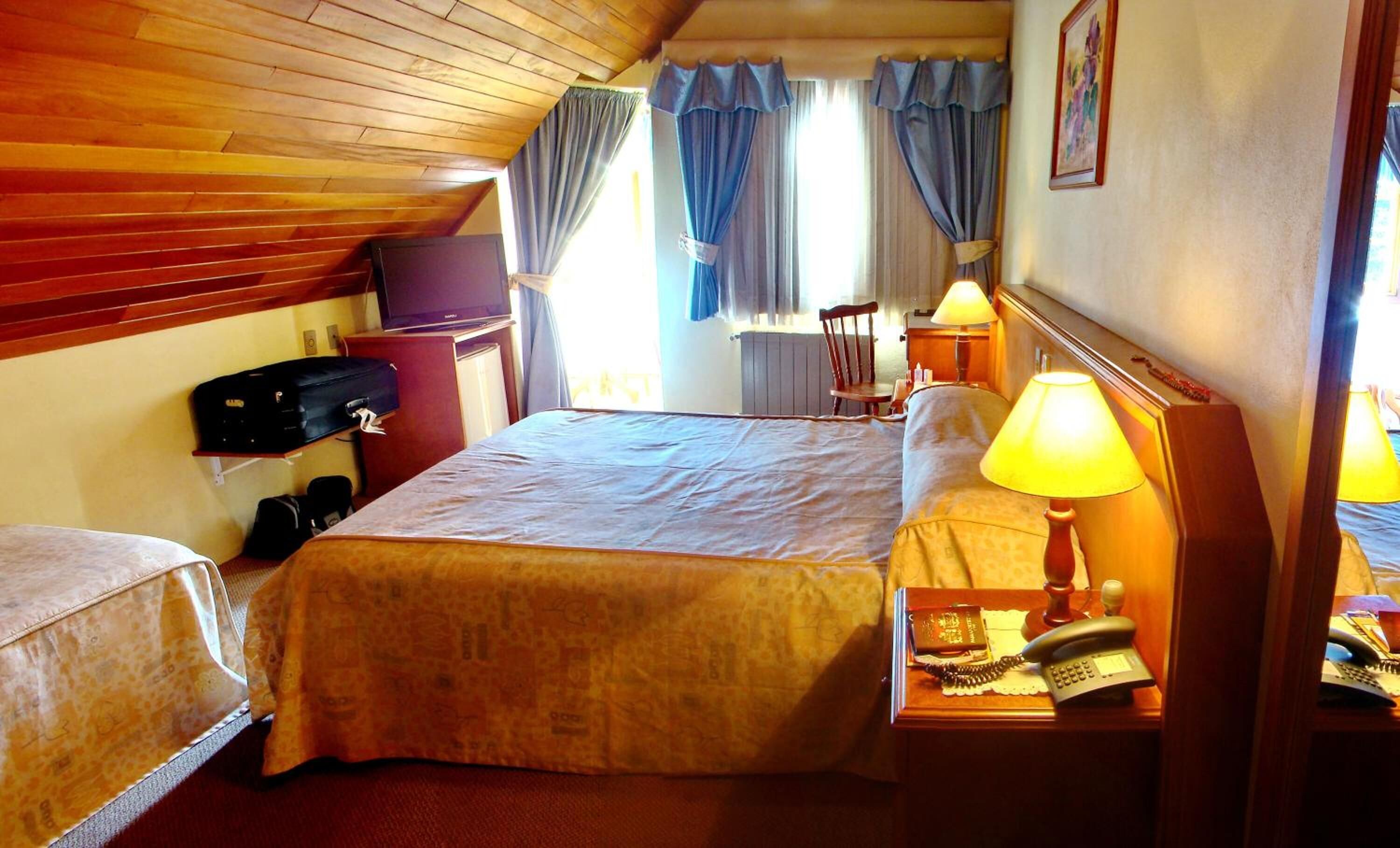 A hotel room with two beds, a television, a desk with a lamp, and a chair.