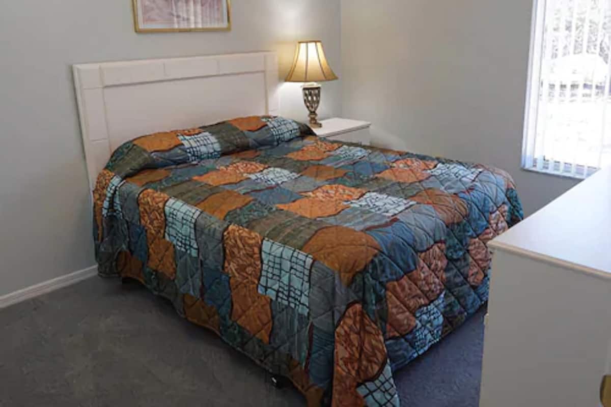 Quarto com cama, mesa de cabeceira, luminária e janela.