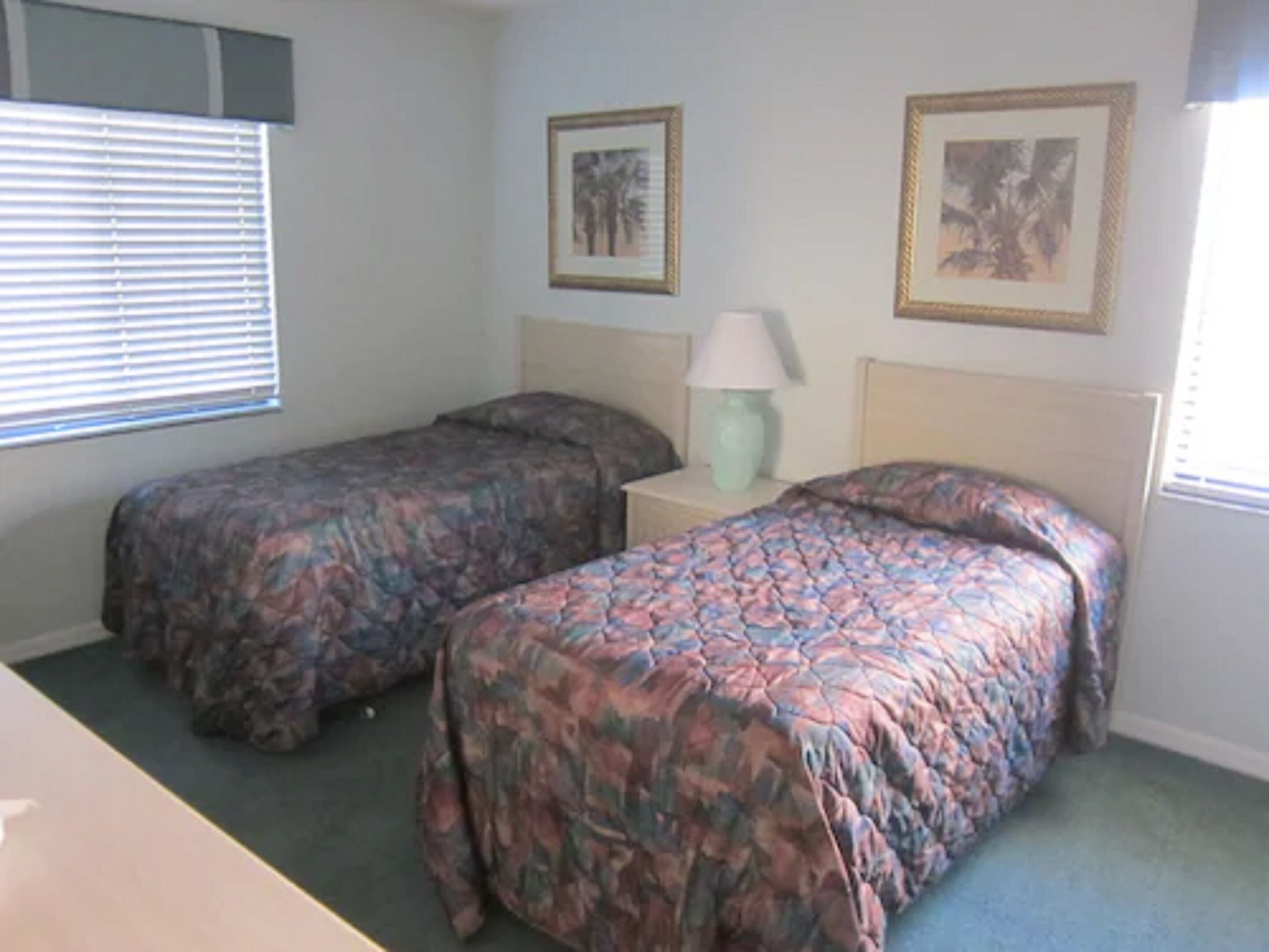 A bedroom with two single beds, a nightstand with a lamp, and two framed pictures on the wall.