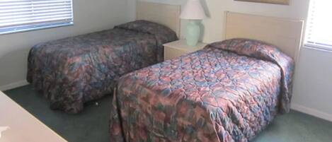 A bedroom with two single beds, a nightstand with a lamp, and two framed pictures on the wall.