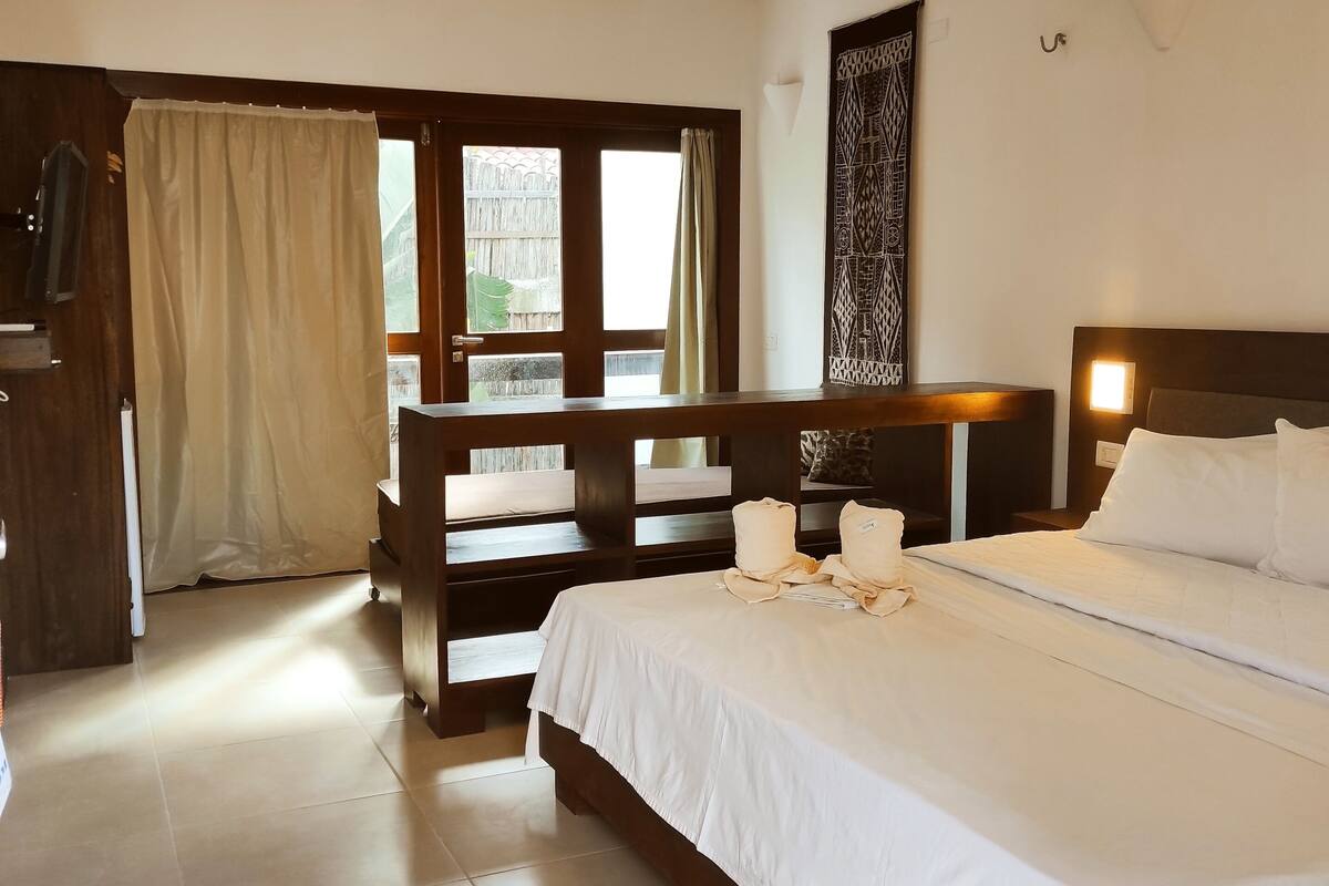 Habitación de hotel con cama, escritorio, silla, ventana con cortinas y puerta.