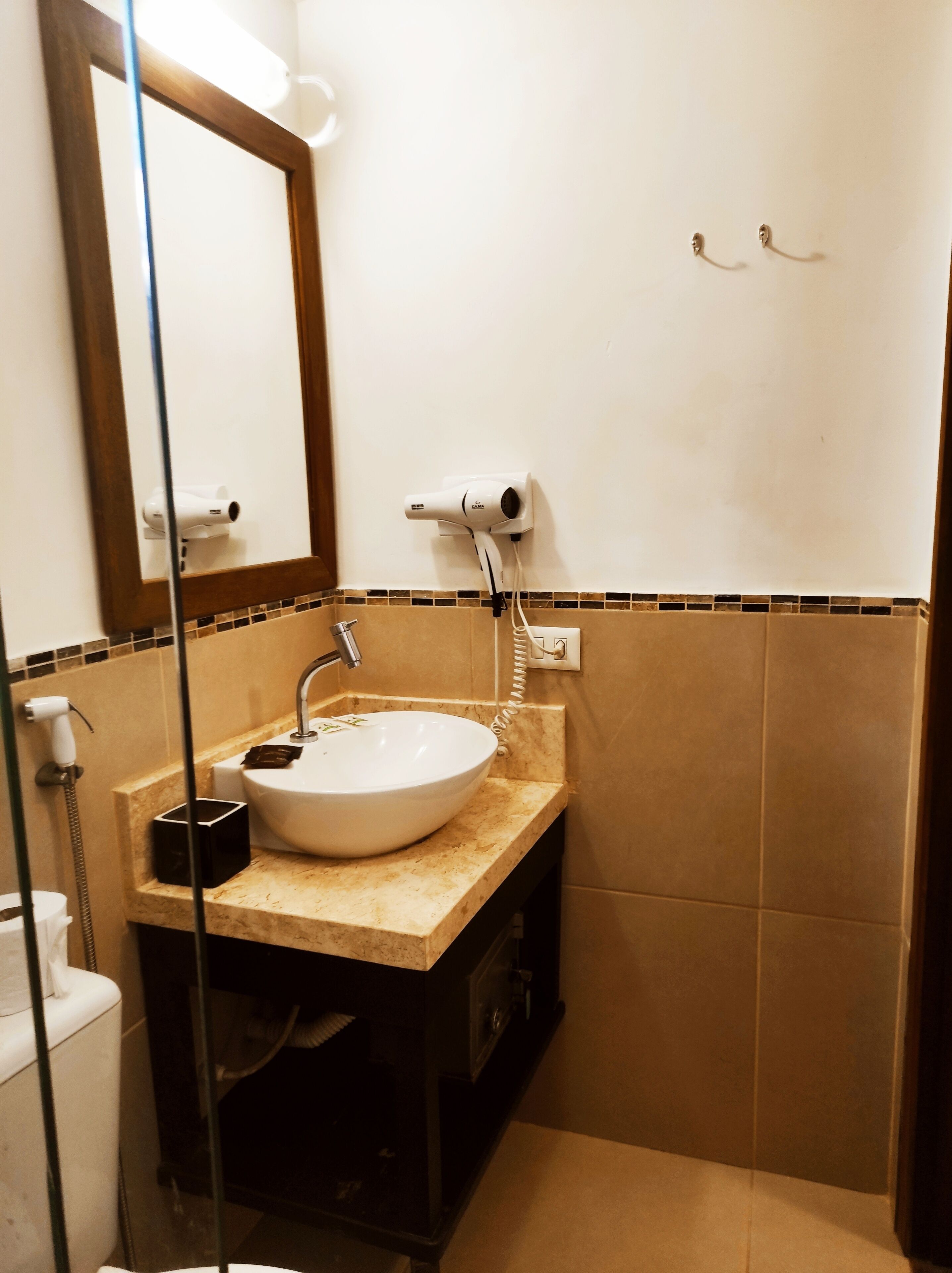 Un baño con lavamanos blanco, espejo, secador de pelo y toallero.