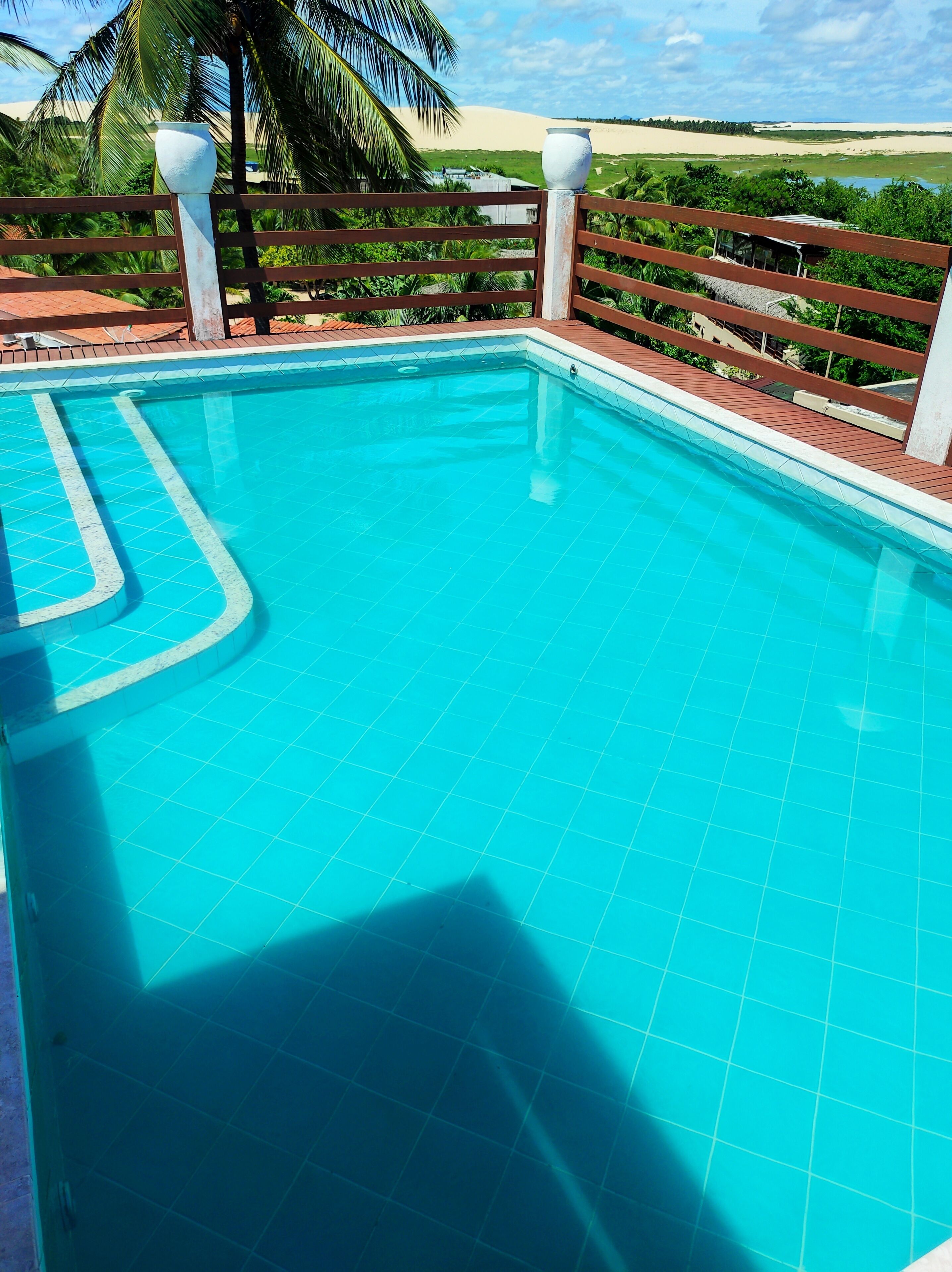 Ein Schwimmbecken mit klaren, blauen Fliesen, umgeben von einer Holzterrasse und Palmen.