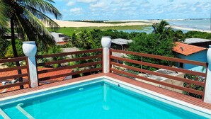 A swimming pool with a wooden deck and a view of a beach and palm trees. - Hotel São Francisco (Jijoca de Jericoacoara)
