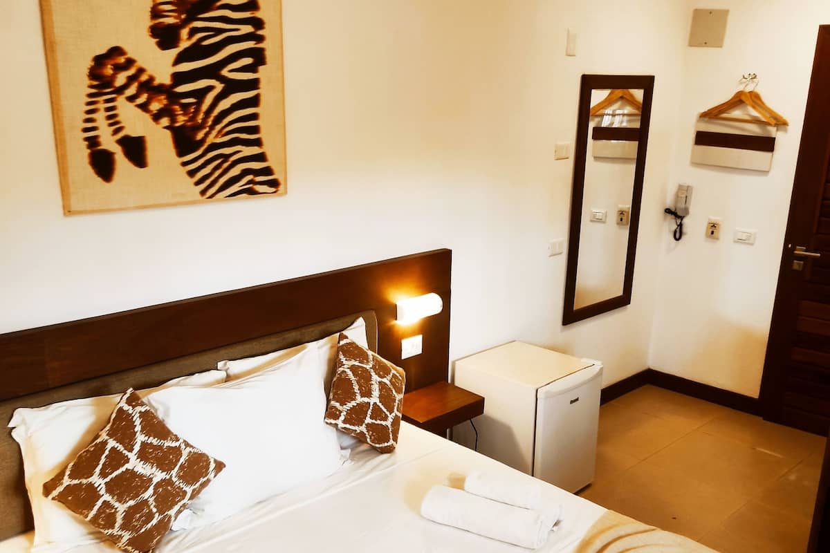 Una habitación de hotel con una cama, una mesita de noche, un espejo, un perchero y un cuadro de cebra en la pared.
