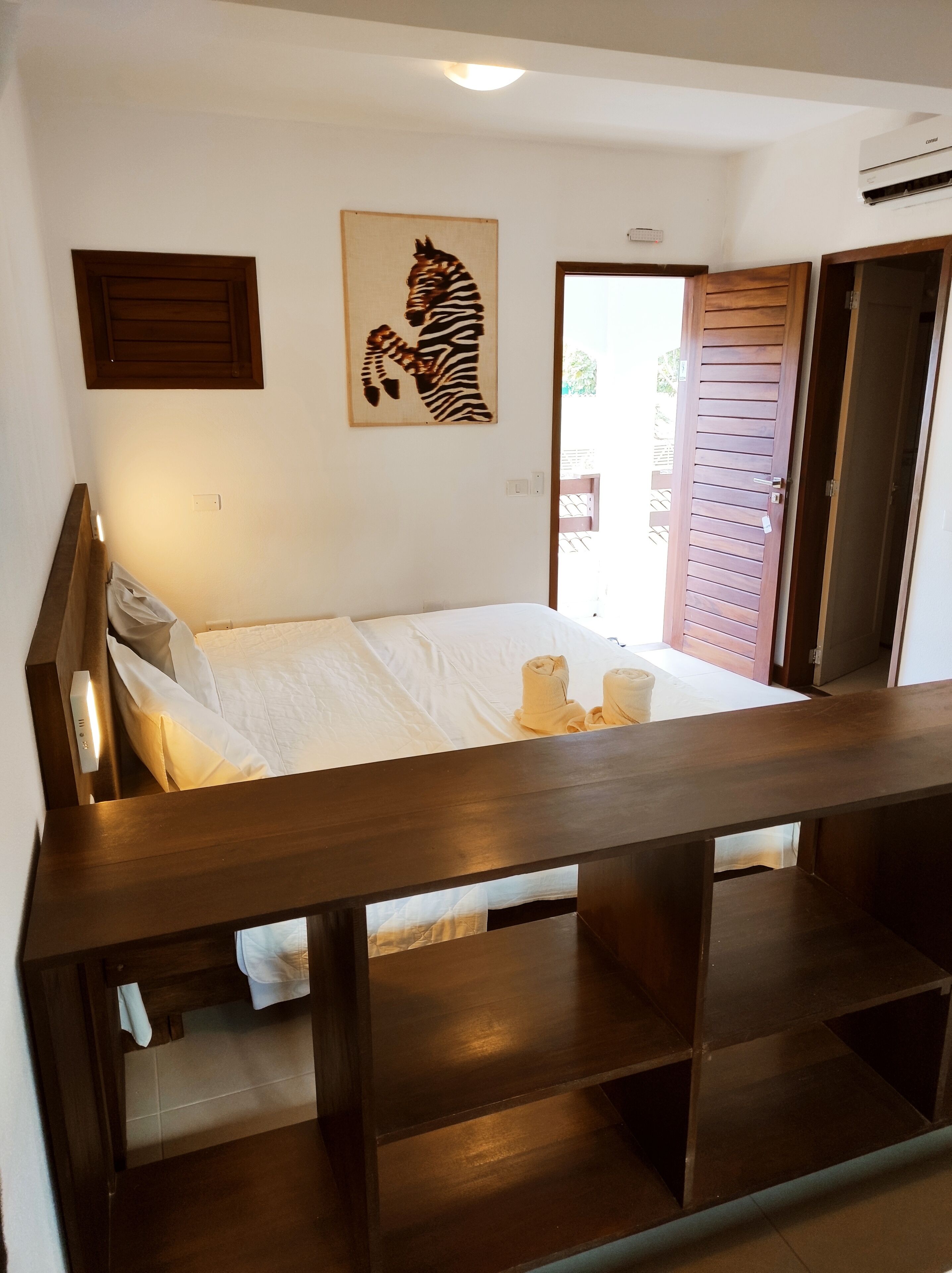 A bedroom with a bed, a zebra artwork on the wall, a wooden door, and a balcony with a view.