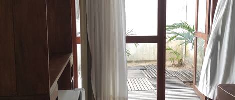 A room with a wooden wardrobe, a white radiator, and a sliding glass door leading to an outdoor area with a wooden deck and plants.