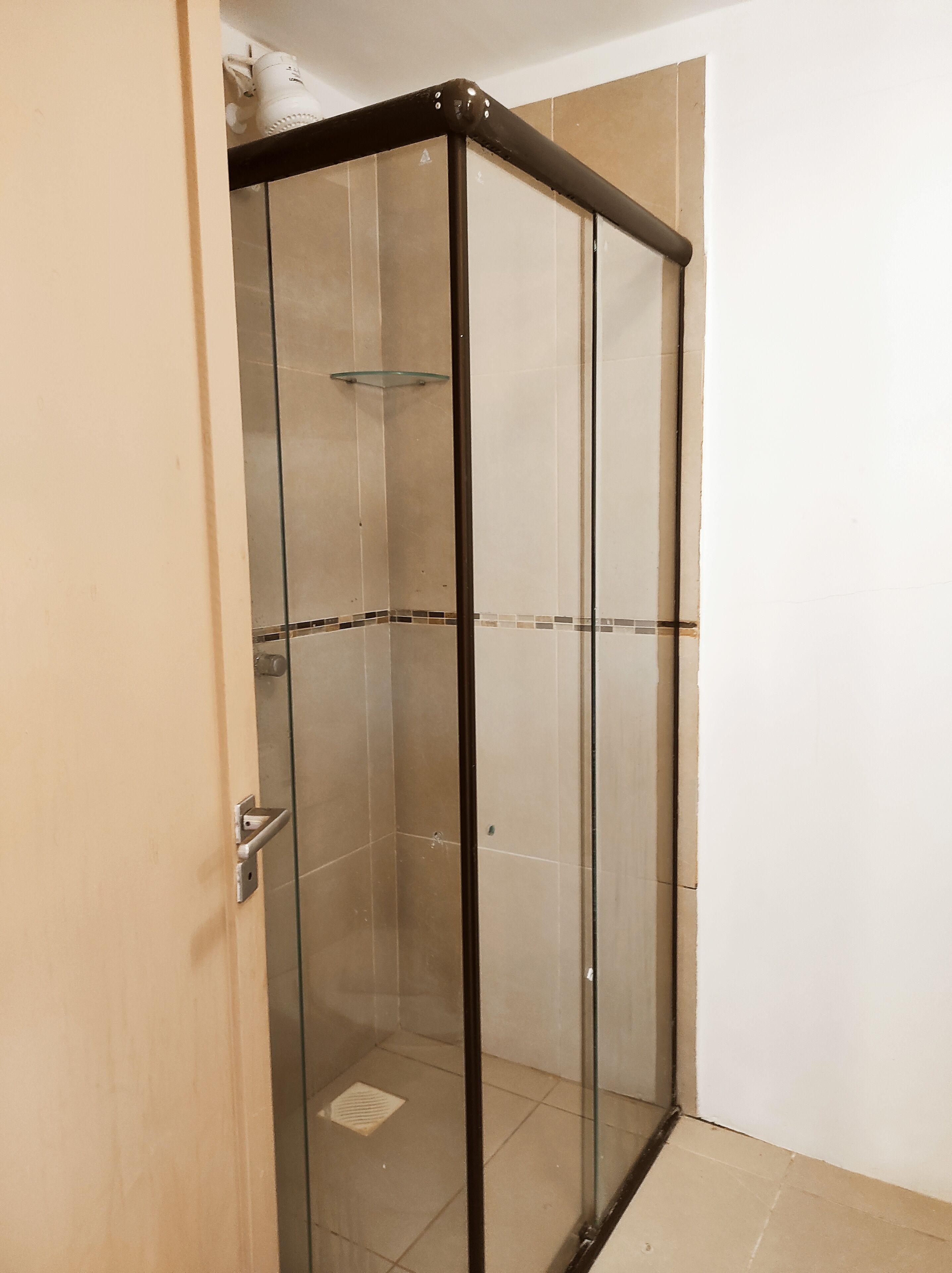 A glass-enclosed shower stall with a metal frame, a glass shelf, and a tiled floor.