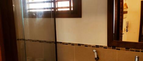 Un baño con cabina de ducha de vidrio, inodoro y lavamanos con espejo.