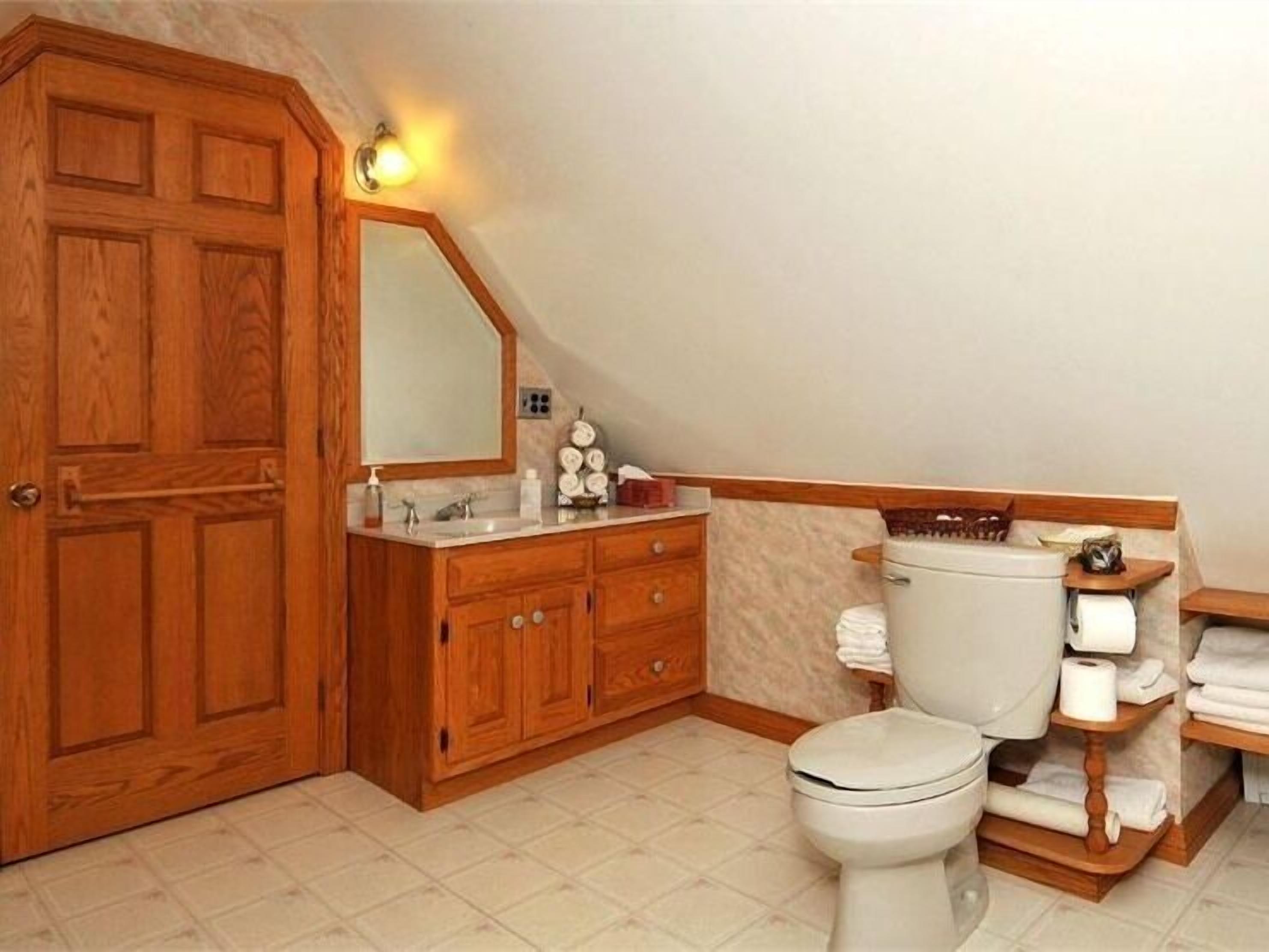 Un baño con muebles de madera, un inodoro blanco y un tocador con espejo.