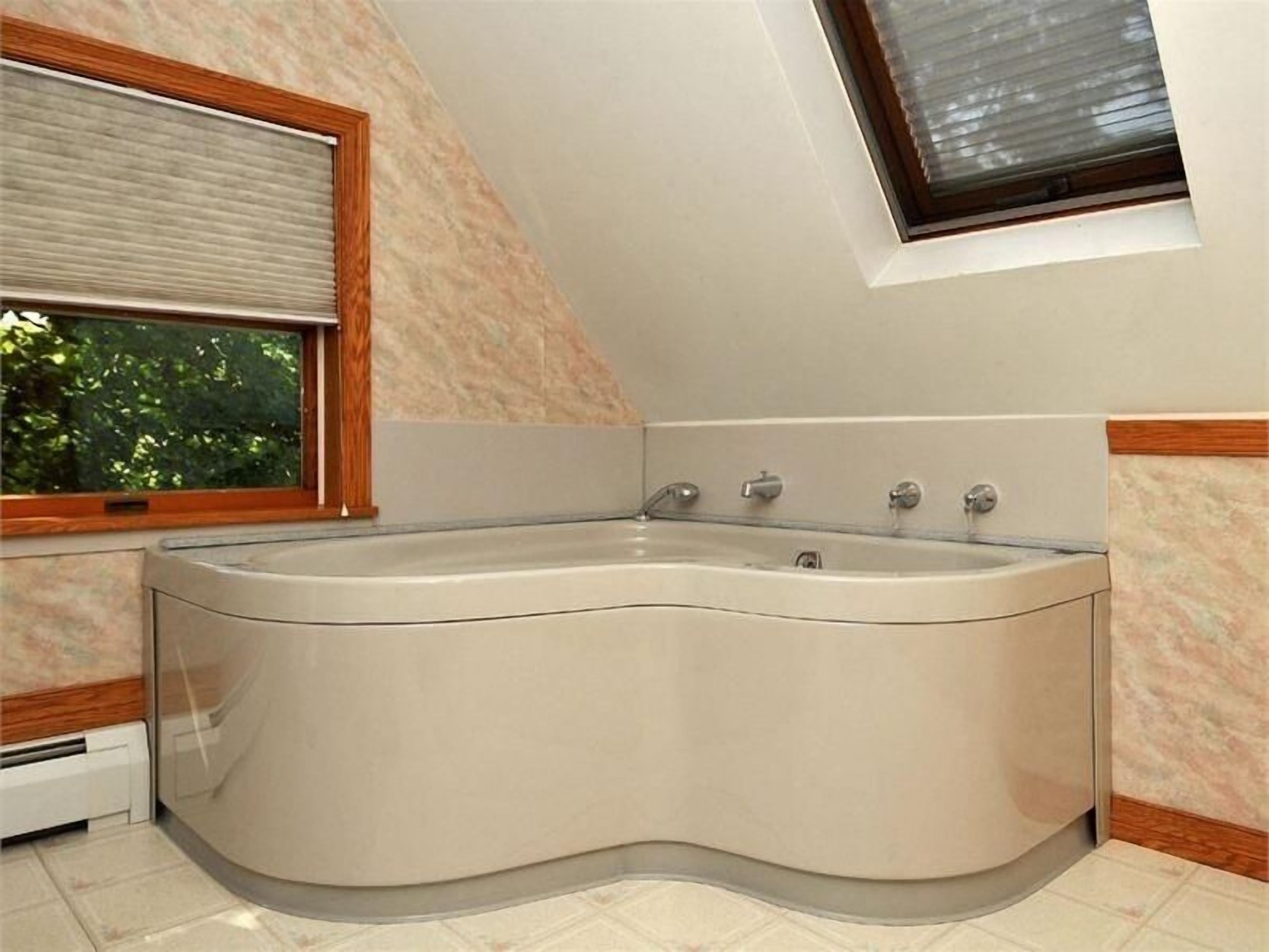 A corner bathroom with a freestanding bathtub, a window with blinds, and a tiled floor.