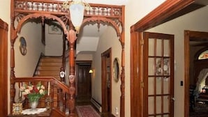 Un escalier en bois orné de sculptures complexes, une petite table sur laquelle est posé un vase de fleurs et un tapis à motifs sur un plancher en bois.