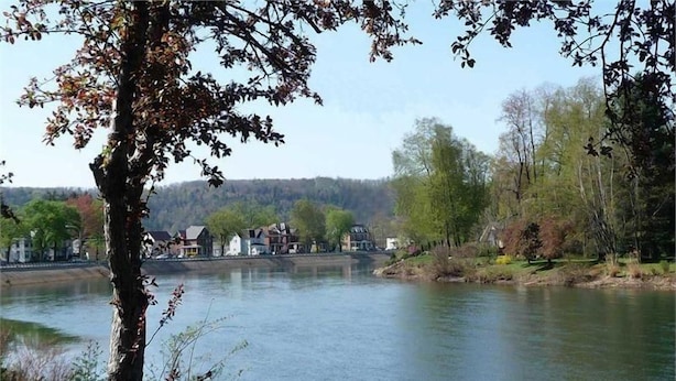 Une rivière bordée de maisons de l’autre côté, entourée d’arbres et de verdure.