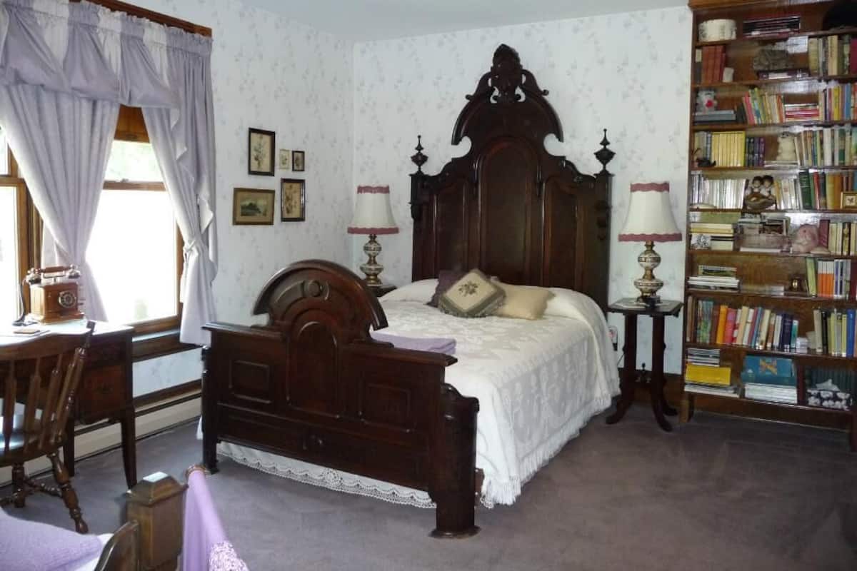Un dormitorio con cama de madera, un escritorio, una estantería y una ventana con cortinas.