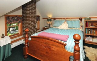 Un dormitorio con una cama con dosel de madera, chimenea de ladrillo, ventana con vistas, mesita de noche y estantería.