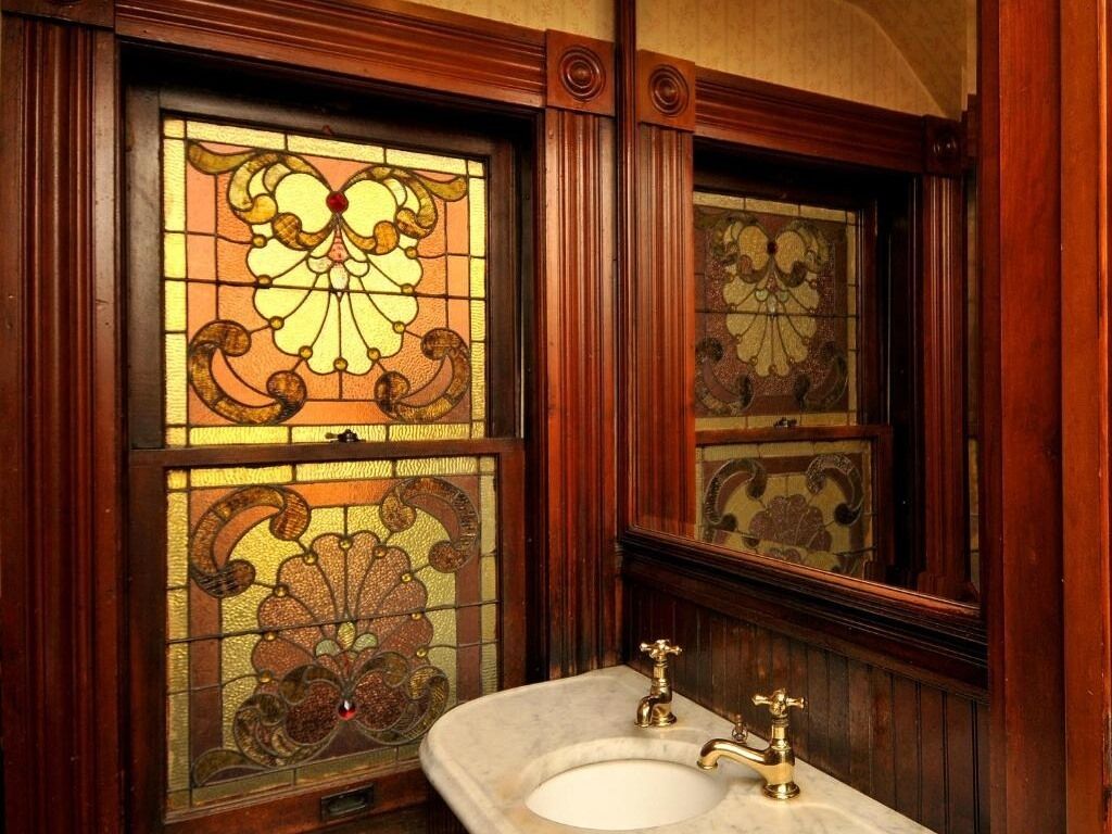 Un baño con lavamanos de mármol, paneles de madera ornamentados y vidrieras.
