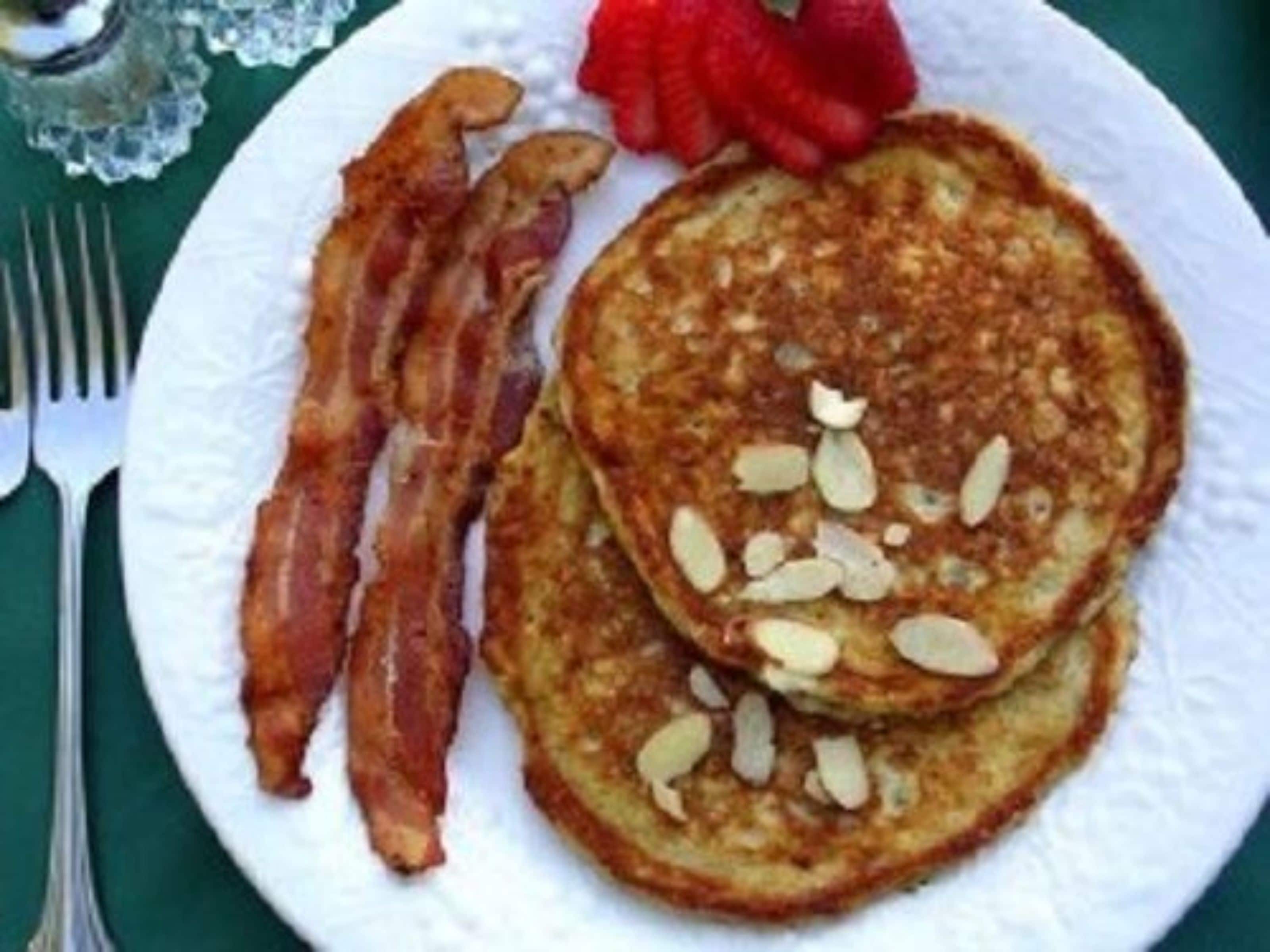 Un piatto con pancakes guarniti con mandorle, accompagnati da pancetta e una fragola.