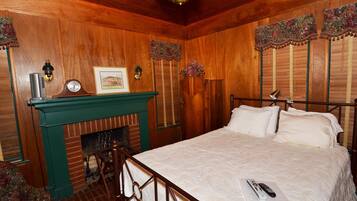 Une pièce avec un plafond en bois, un lit recouvert de draps blancs, une cheminée et une horloge posée sur la manteau de la cheminée.