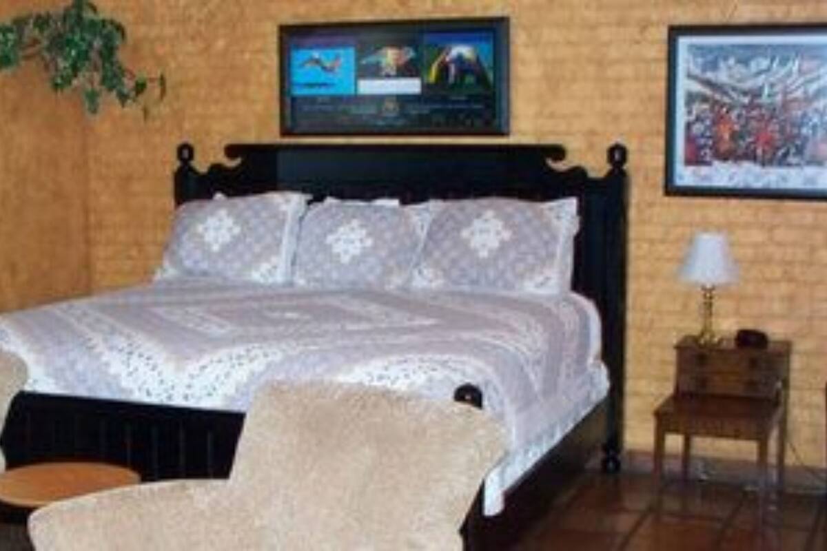 Quarto com uma cama, dois poltronas, uma mesinha e duas televisões fixadas na parede.
