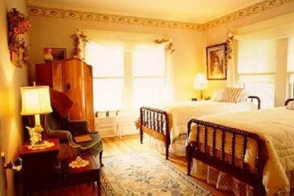 Quarto tradicional com cama de madeira, mesa de cabeceira, cômoda e janela com cortinas.